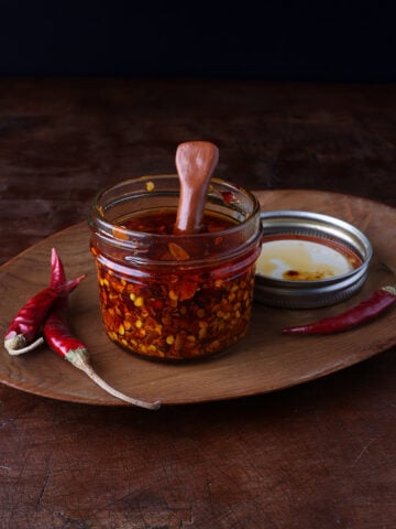 Small clay spoon resting in a glass jar of chile de arbol oil.