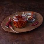 Chile de arbol oil in a glass jar on a wooden tray.