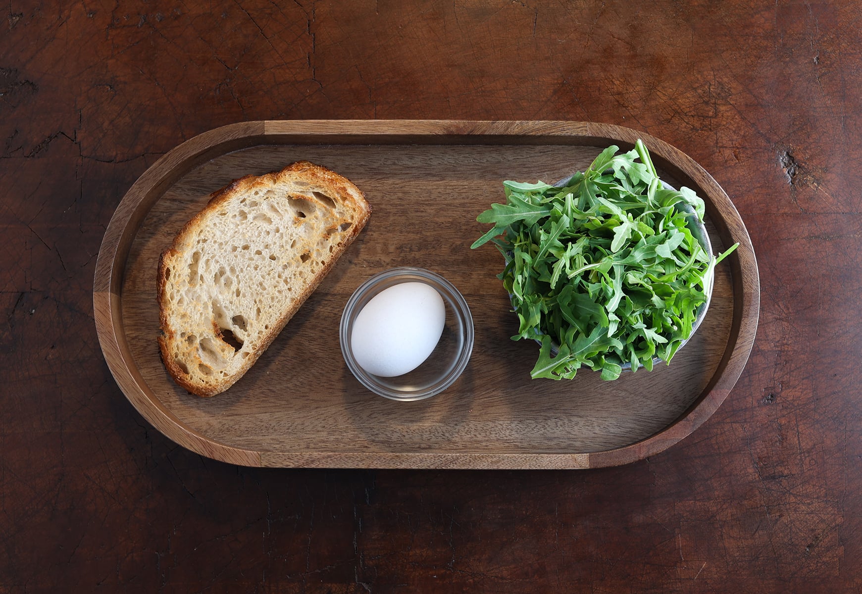 toast, egg, arugula on a wood platter