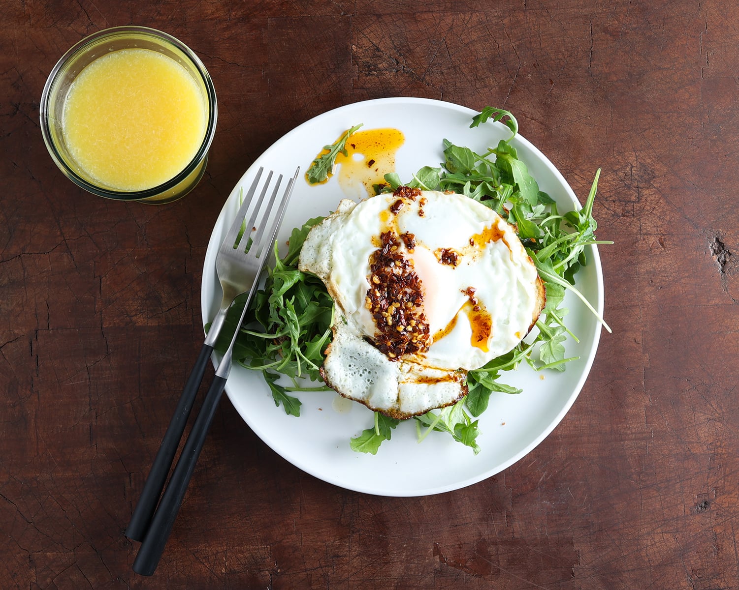 Chile de arbol oil drizzled over a fried egg laying on a bed of greens.