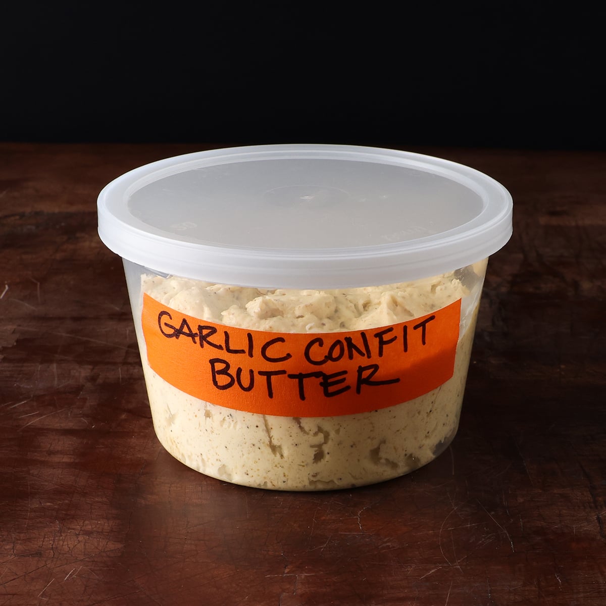 Small plastic container with a lid filled with homemade garlic confit butter.