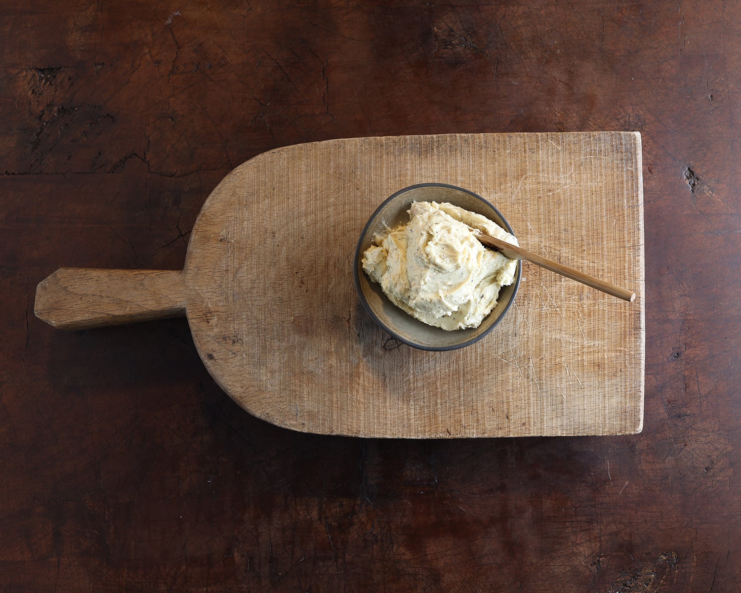 Garlic confit in bowl sitting on a wooden cutting board.
