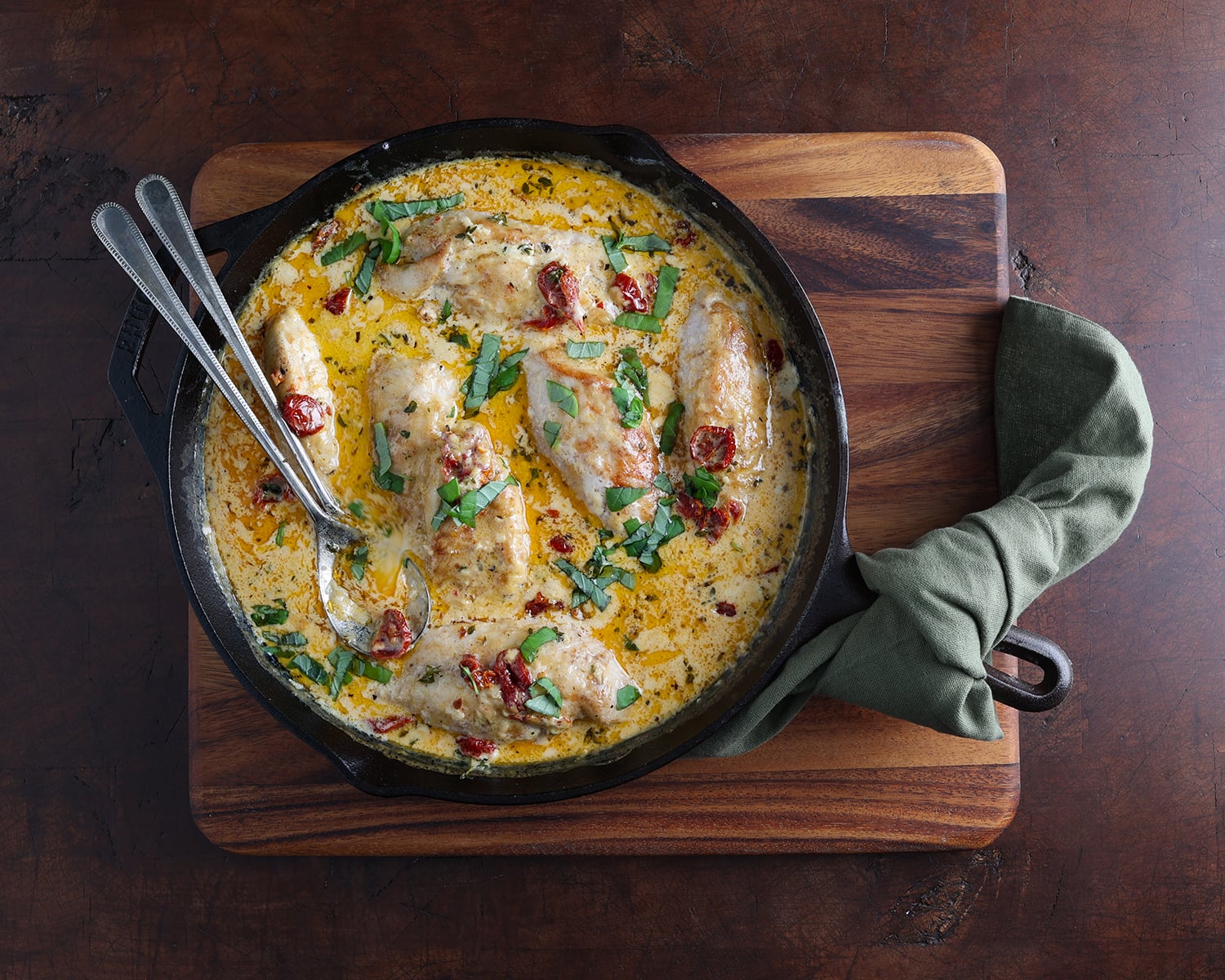 Green cloth napkin resting around the handle of a cast iron skillet serving Creamy Parmesan Sundried Tomato Marry Me Chicken.