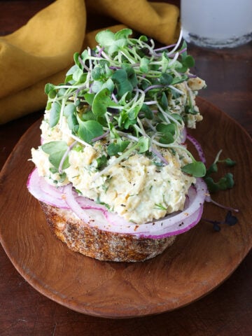 Microgreens topping an open faced sandwich topped with smashed chickpea salad.