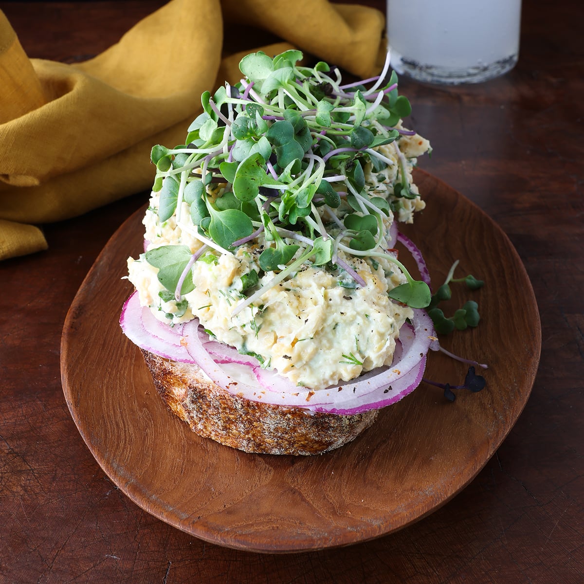 Microgreens topping an open faced sandwich topped with smashed chickpea salad.