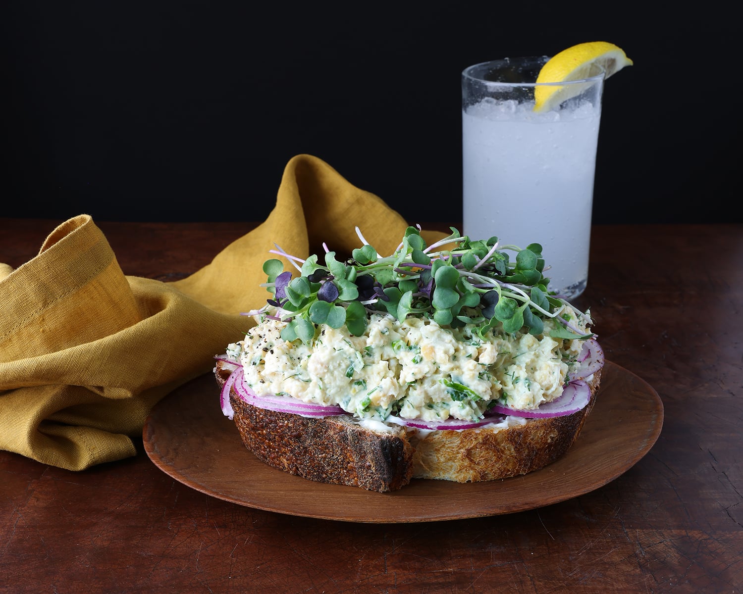 Open faced smashed chickpea salad sandwich topped with microgreens.