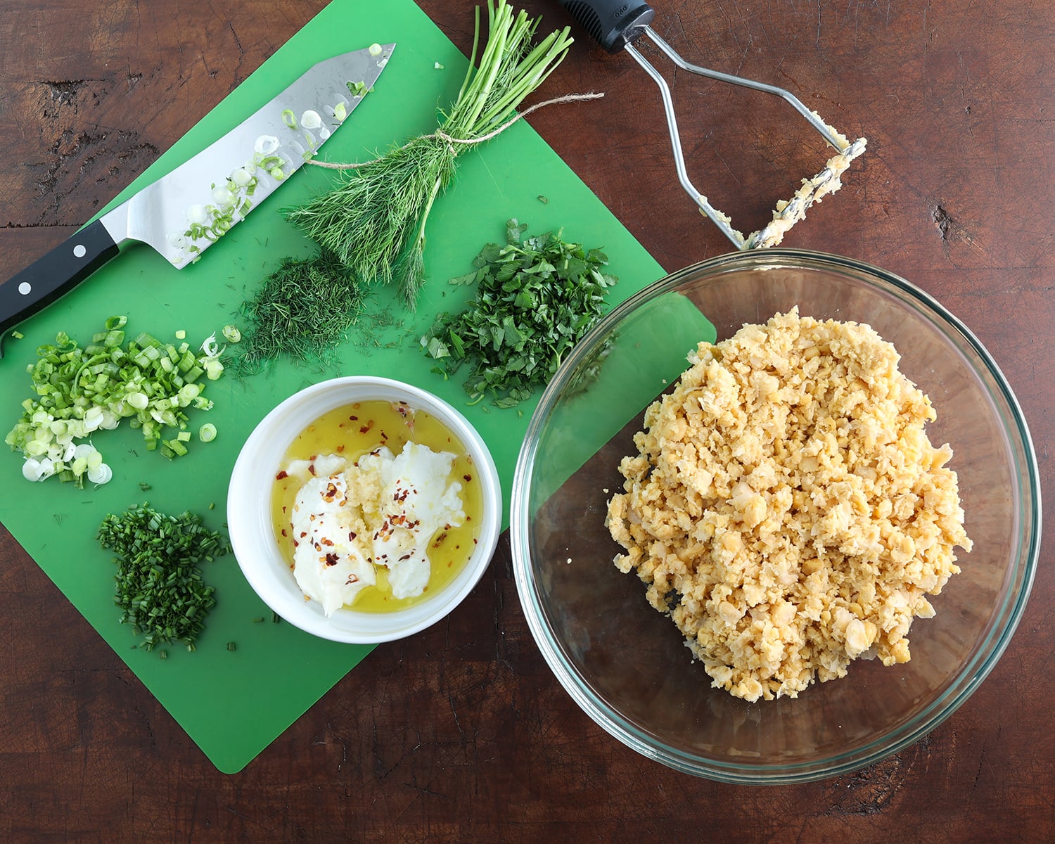 Cutting board with chopped ingredients on it to make a chickpea salad with dressing ingredients measured out in a bowl.