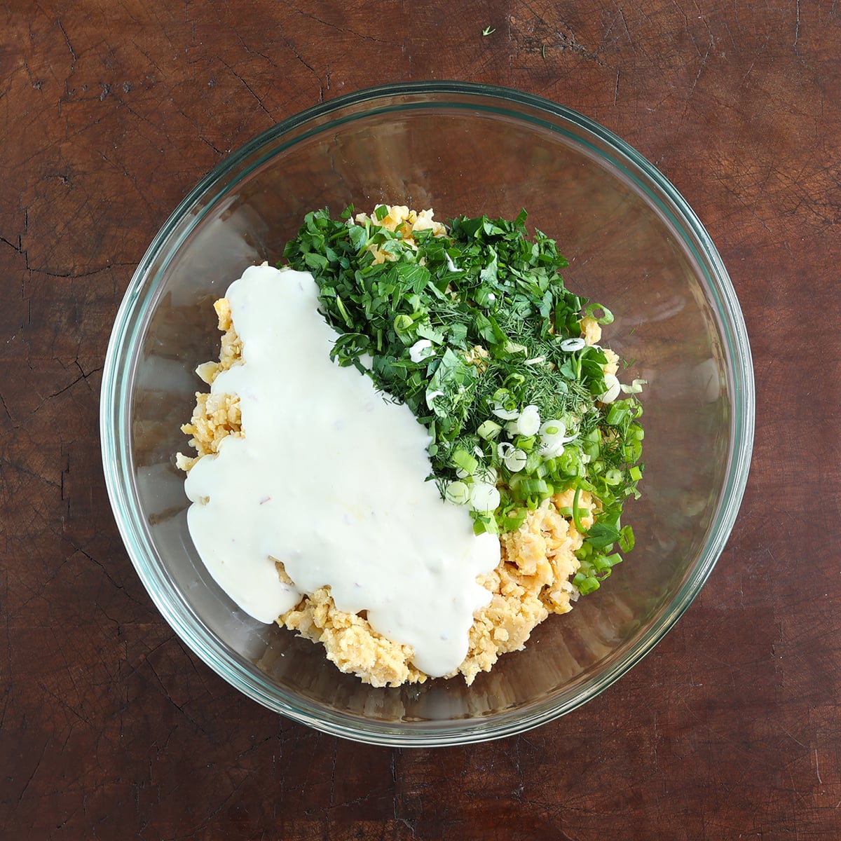 Mashed chickpeas and other ingredients added to a glass bowl without combining.