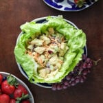 Curry Cashew Chicken Salad in a lettuce cup on a plate with grapes on a wood table