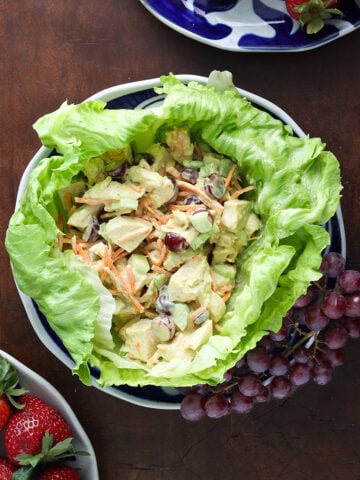 Curry Cashew Chicken Salad in a lettuce cup on a plate with grapes on a wood table