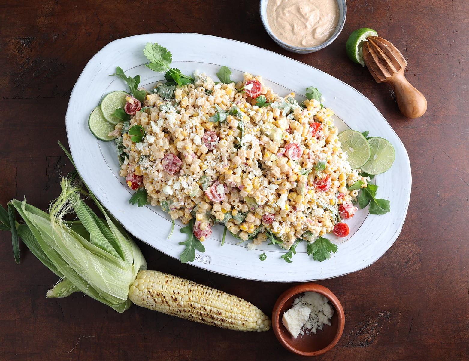 Overhead view of a grilled corn pasta salad with queso fresco in a small bowl next to the plate and some sprinkled on top.