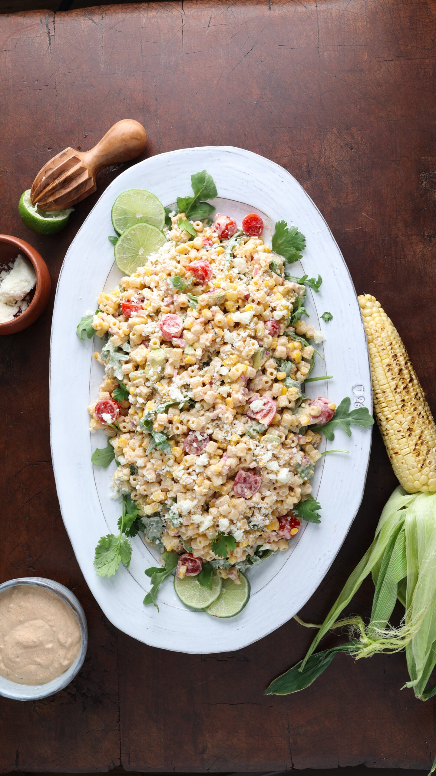 Grilled corn and pasta salad with lime wedges garnished on either side.