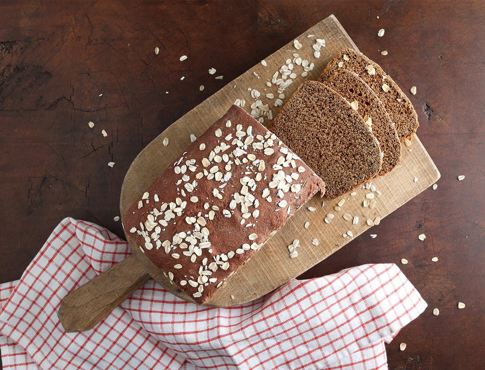 Honey Molasses Brown Bread on cutting board with sprinkled oats and a kitchen towel on a wood butcher block