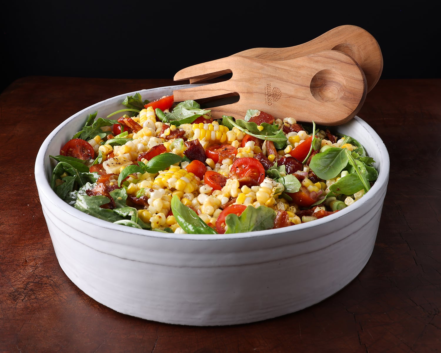 BLT Corn Salad in a white round ceramic bowl with wooden serving spoons