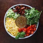 Close up of a BLT corn salad added to a round container, chopped and sliced but not combined with a vinaigrette dressing in the middle.
