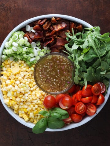 Close up of a BLT corn salad added to a round container, chopped and sliced but not combined with a vinaigrette dressing in the middle.