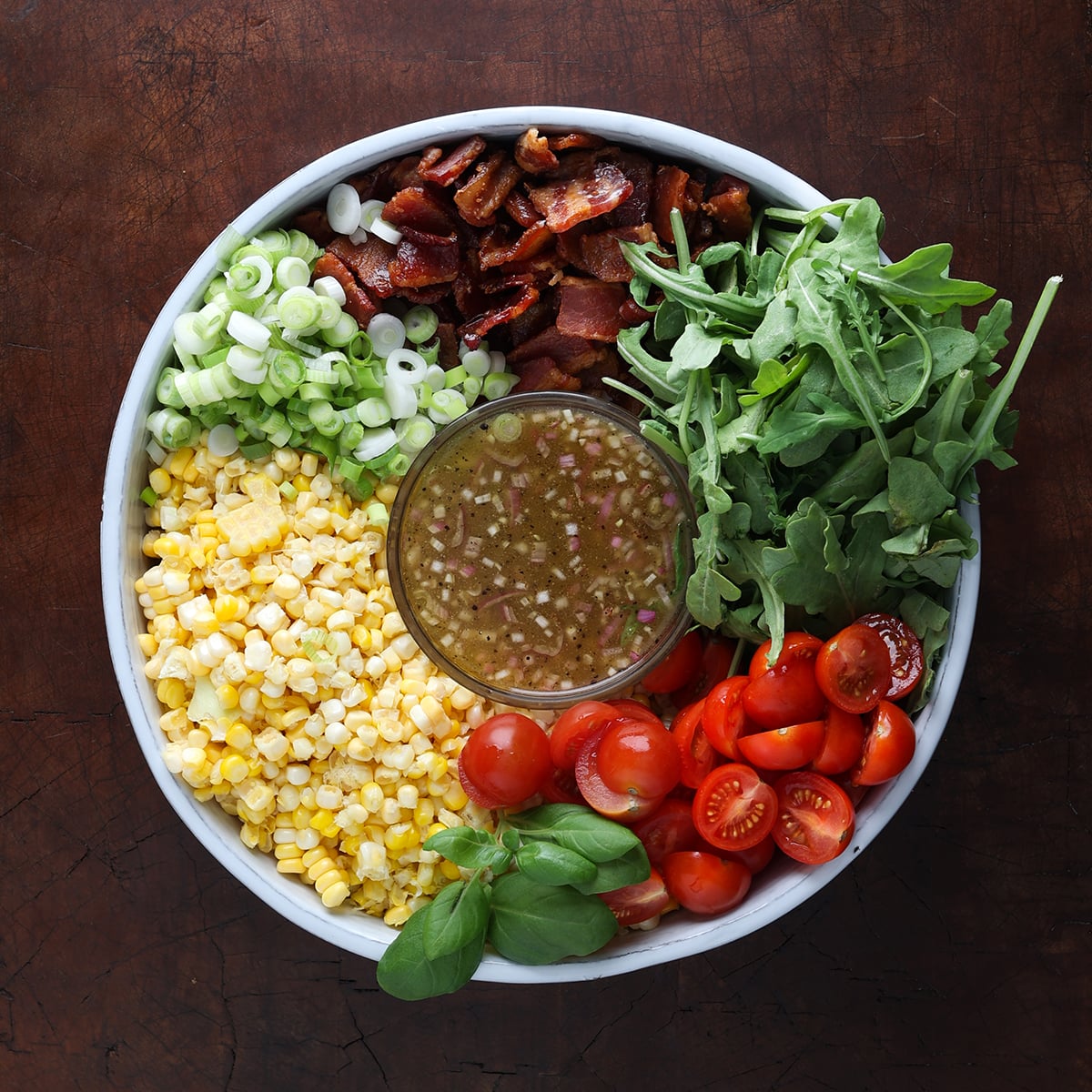 Close up of a BLT corn salad added to a round container, chopped and sliced but not combined with a vinaigrette dressing in the middle.