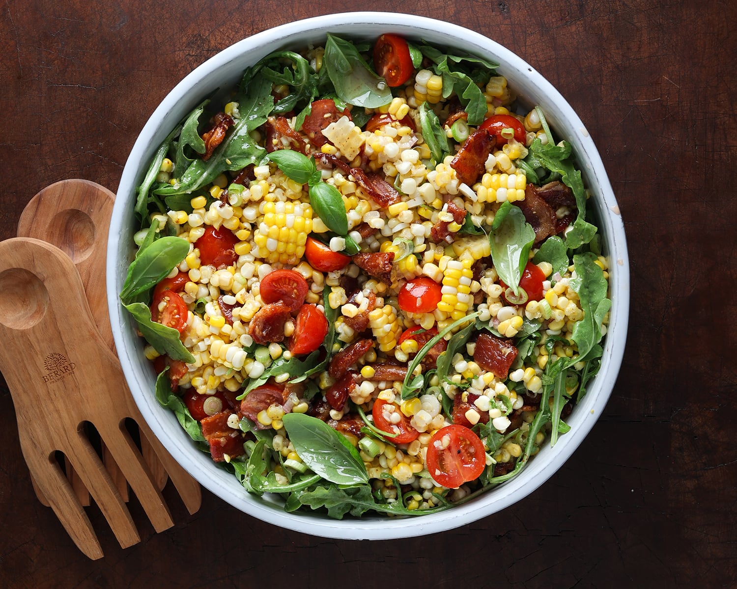 BLT corn salad with wooden tongs resting on the side.