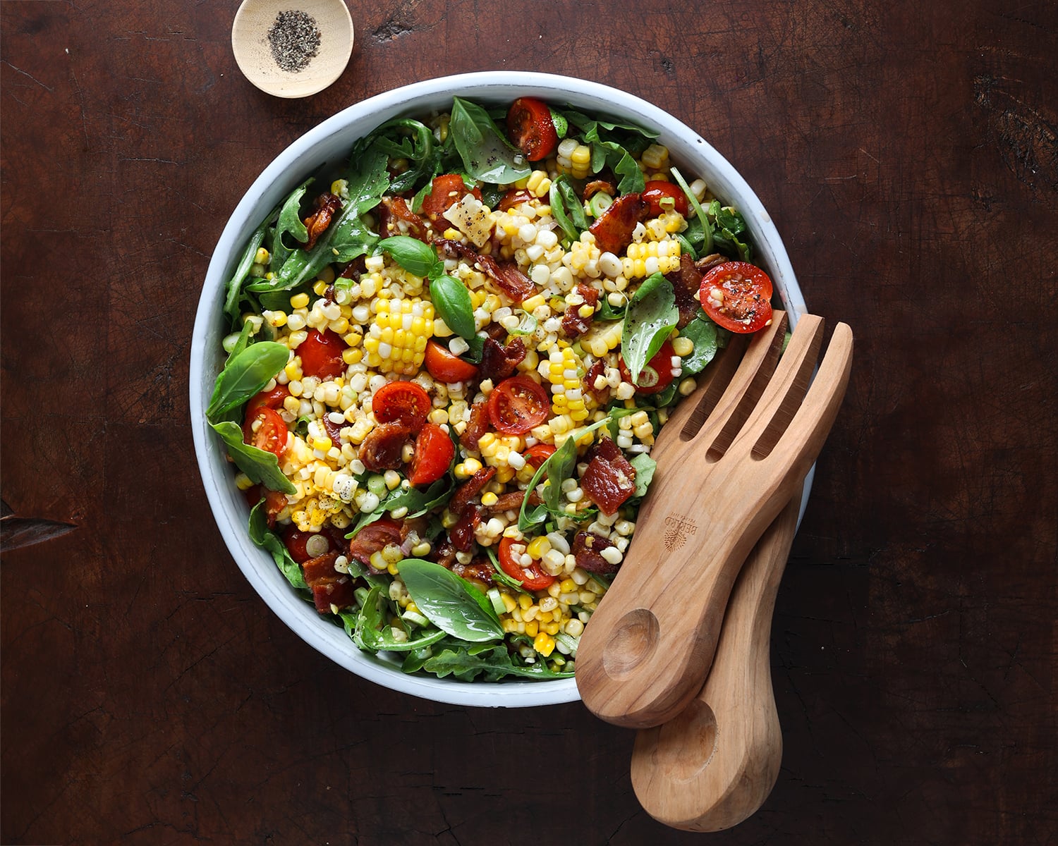 Wooden tongs resting in the BLT corn salad mixture.