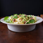 pasta carbonara in a serving dish, side view with english peas, prosciutto and watercress