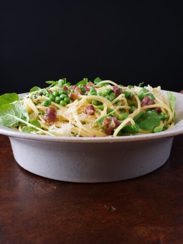 pasta carbonara in a serving dish, side view with english peas, prosciutto and watercress