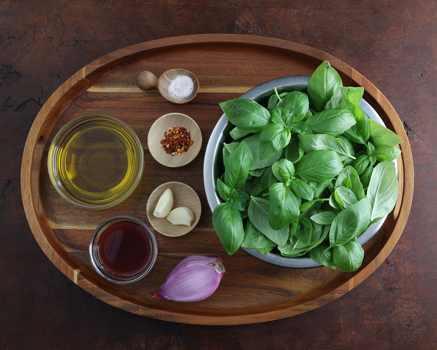 Ingredients for preparing basil vinaigrette laid out on a wooden platter.