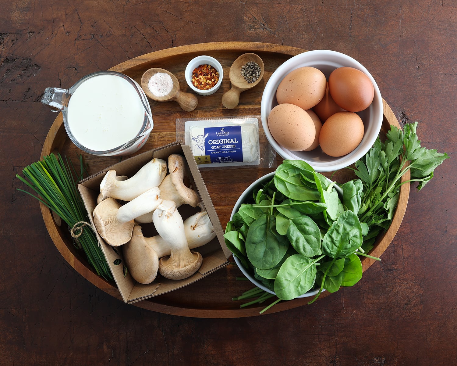 Ingredients to prepare a potato crust quiche with king trumpet mushrooms and goat cheese laid out on a wooden serving tray.