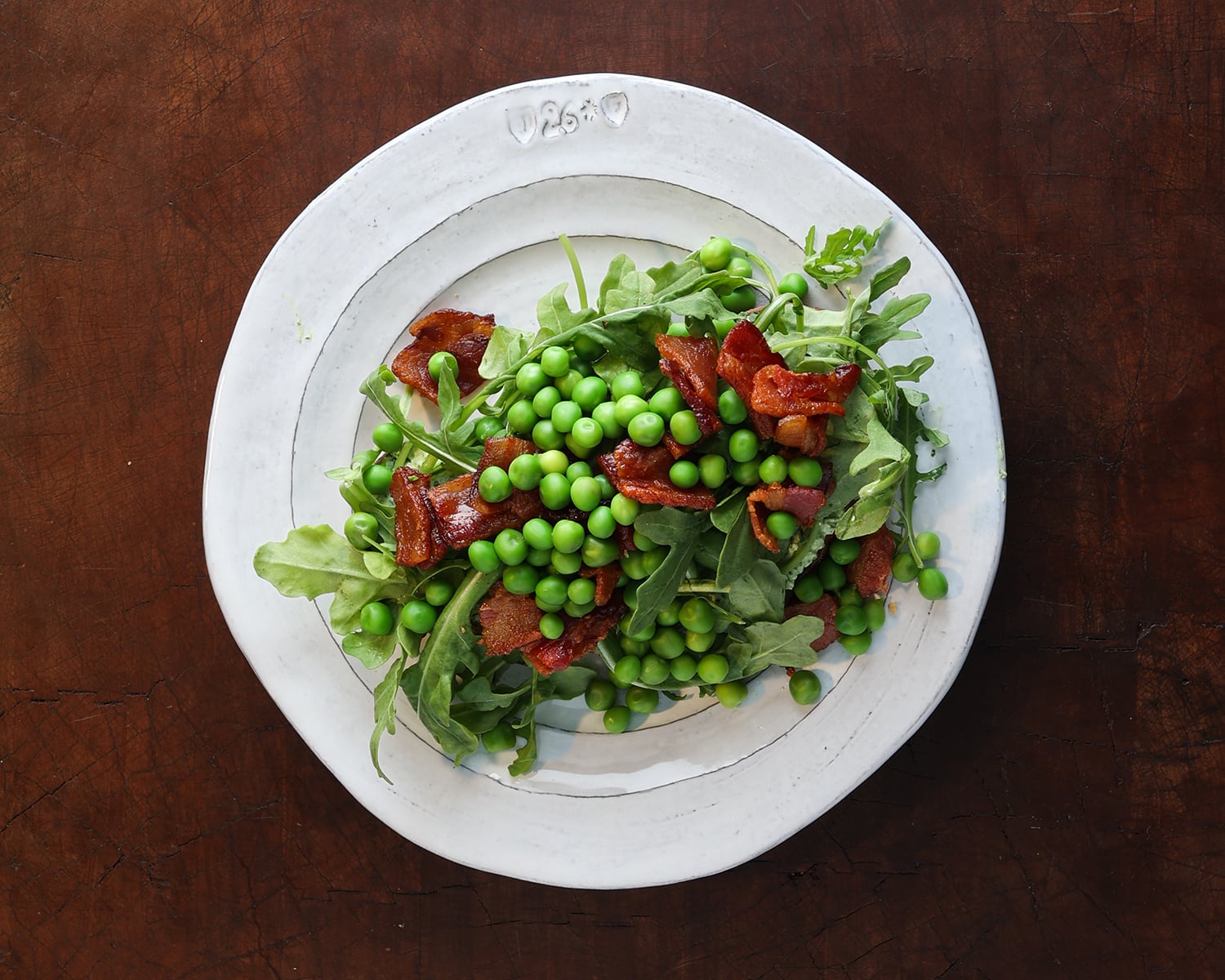 Top view of a piece of toast with herbed goat cheese, crispy bacon pieces, arugular, and then some English peas.