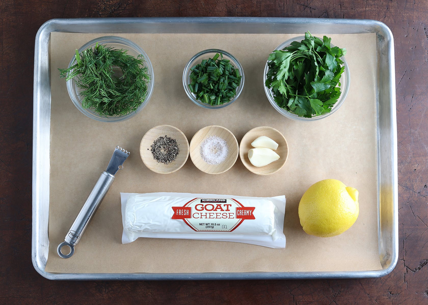 Ingredients needed to prepare herbed goat cheese laid out on a baking sheet.