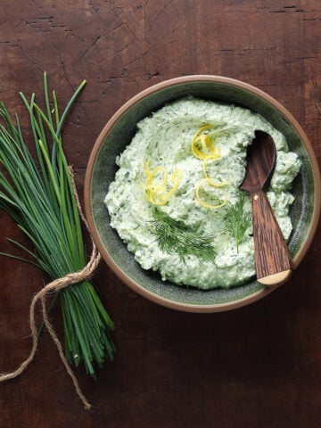 Herbed goat cheese served in a bowl with fresh chives laying next to the dish.