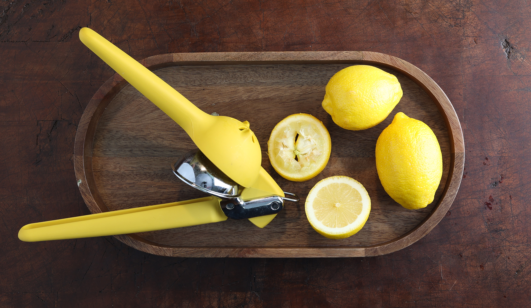 Lemons and a lemon juicer on a wood platter on a wood butcher table