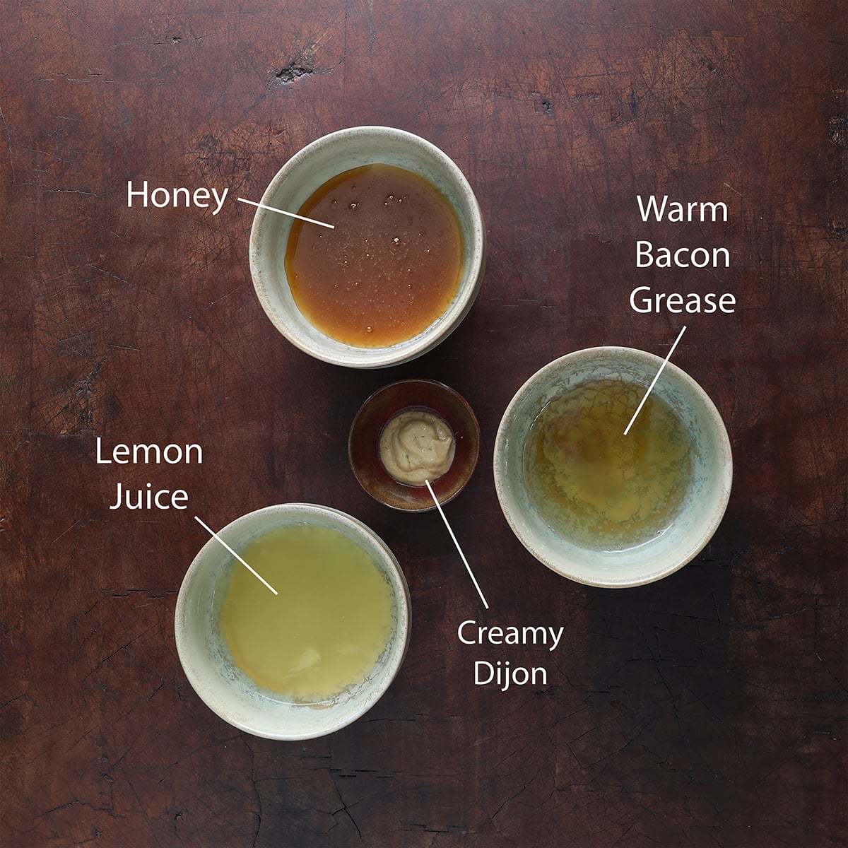Ingredients measured out and displayed in individual small bowls that are used to prepare a honey lemon bacon dressing.