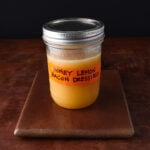 Closed lid on a pint glass jar with tape that says Honey Lemon Bacon Dressing and shows an orangey liquid inside.