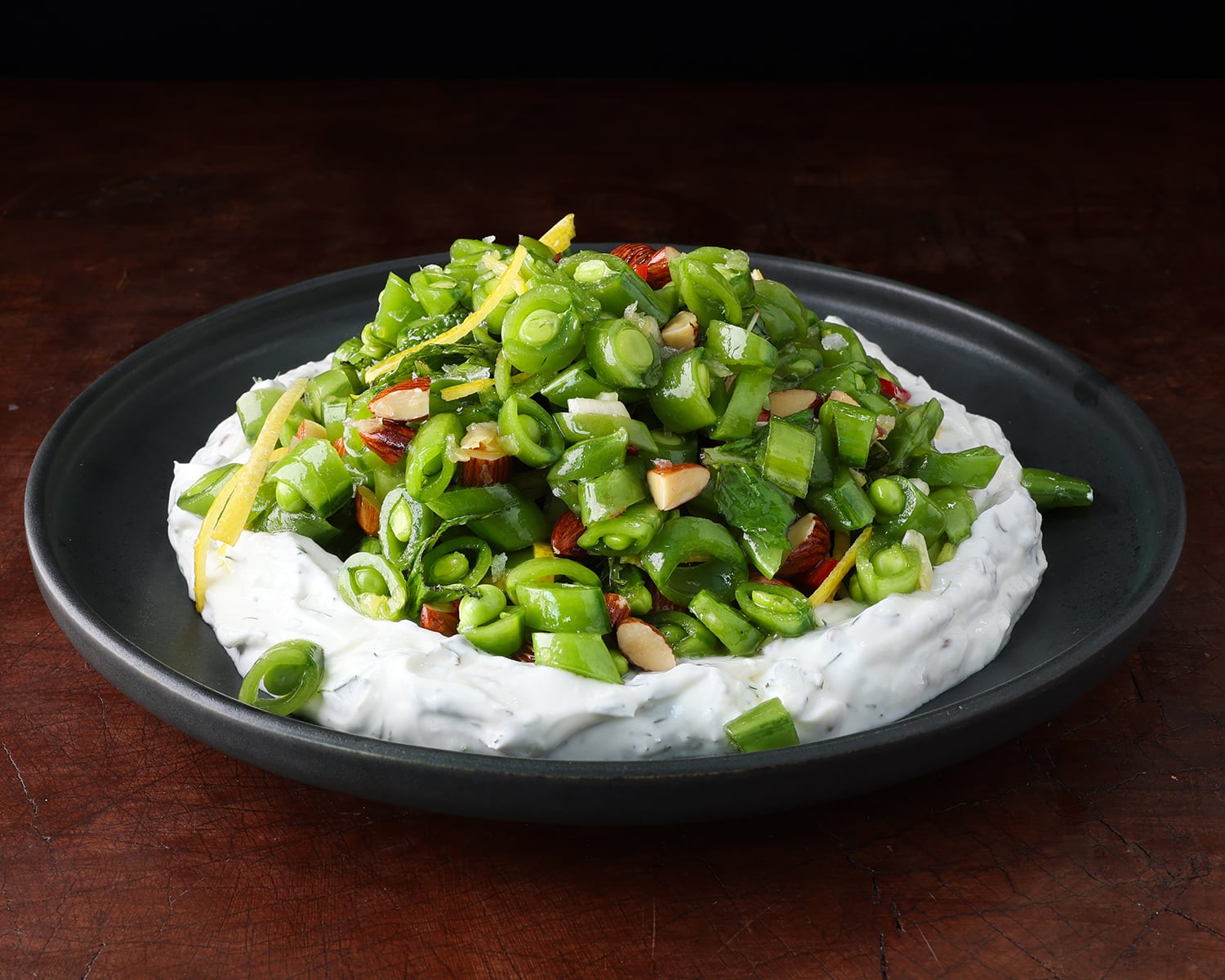 Side view of a spring sugar snap pea salad topped high over a bed of herby Greek yogurt.