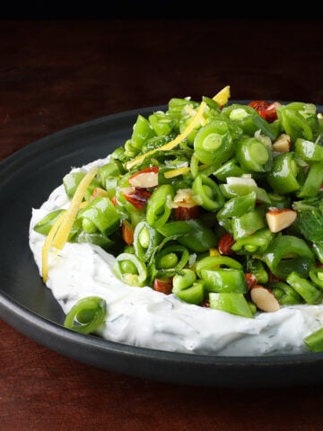 Herby Greek Yogurt on a plate topped with a spring sugar snap pea salad.