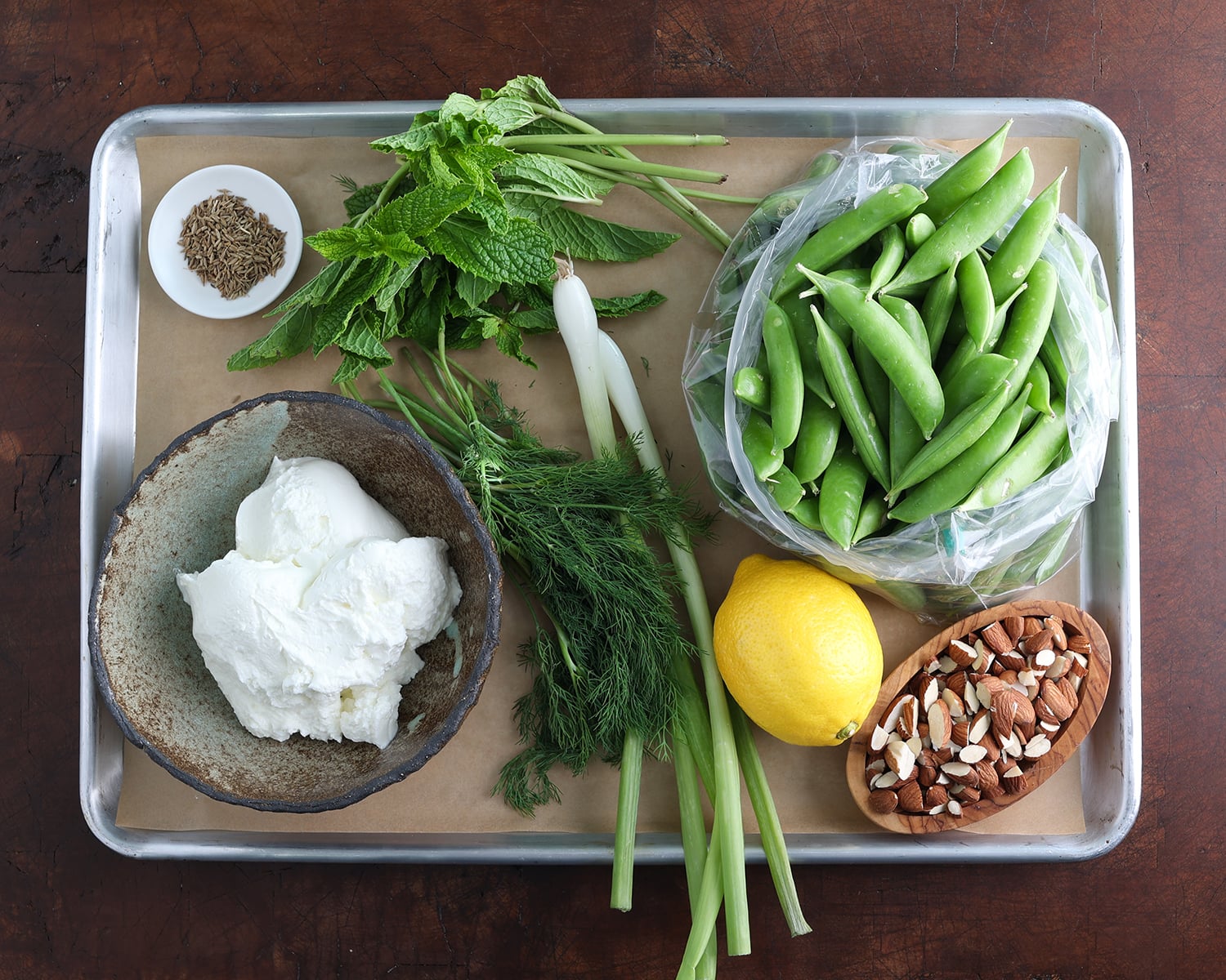 Fresh ingredients on a baking sheet that make up a spring sugar snap pea salad with Greek yogurt.