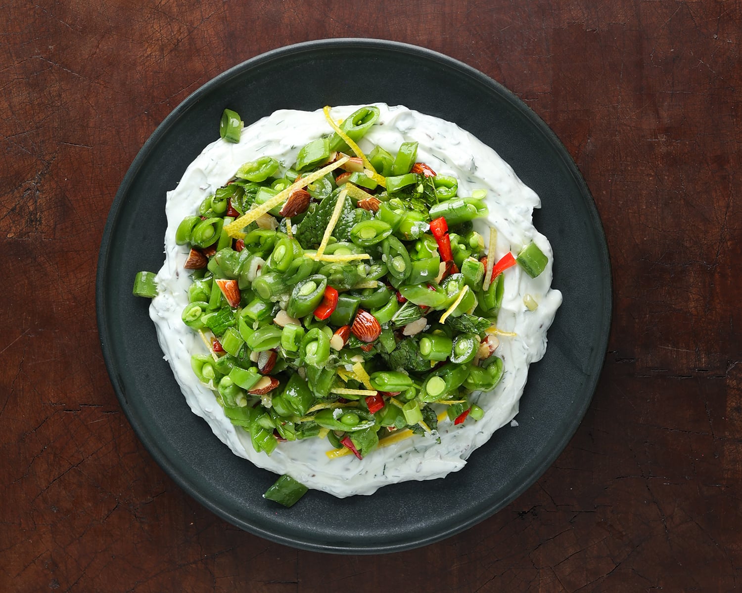 Herby Greek Yogurt on a plate topped with a spring sugar snap pea salad.