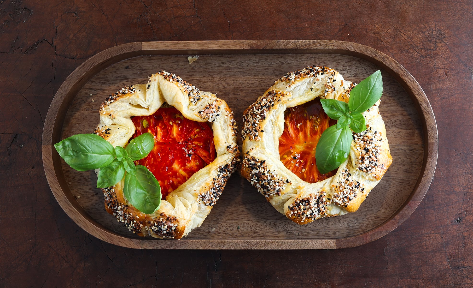 Top view of two freshly baked tomato galettes served on a wooden tray.