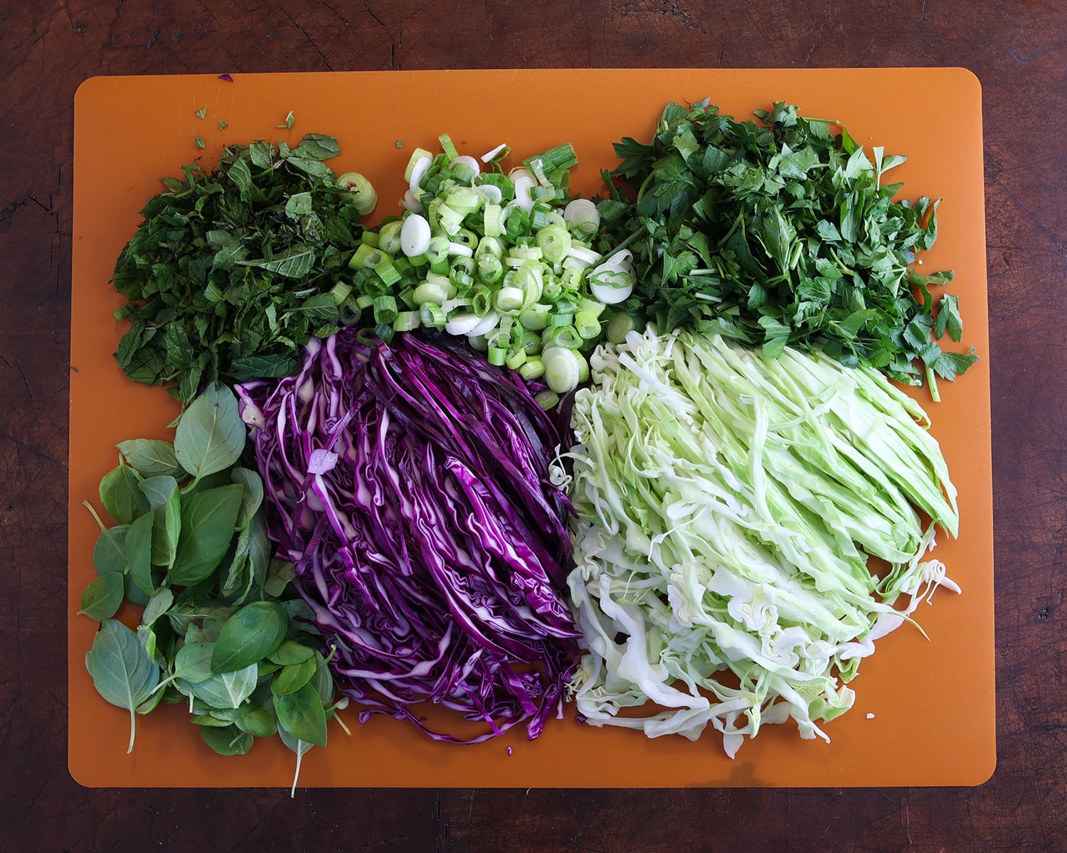Fresh sliced ingredients - cabbage, fresh herbs, etc on a cutting board to add to a chicken rice vermicelli salad.