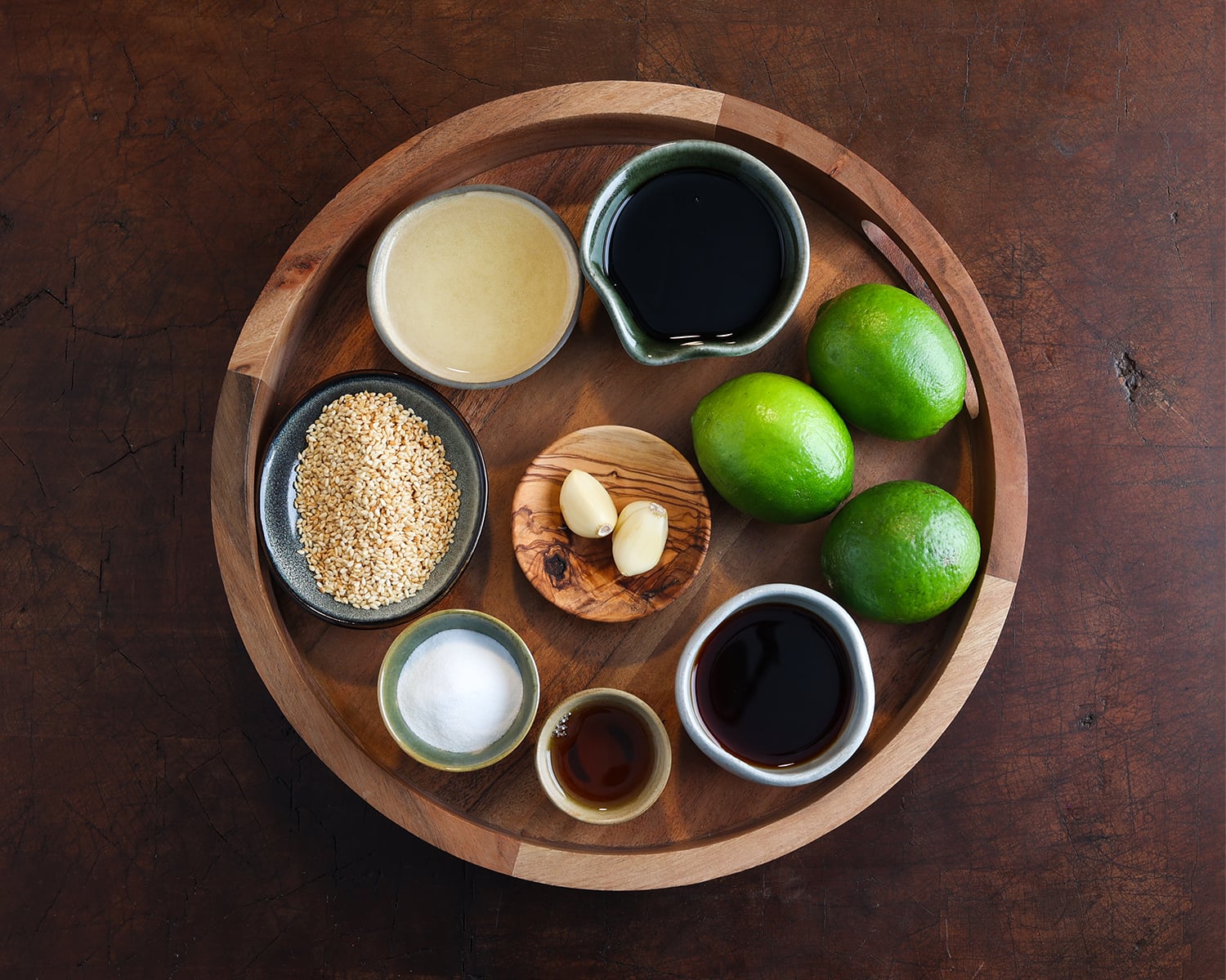 Measured out ingredients in small dishes that are laid out on a wooden trivet to prepared a lime based dressing for a chicken vermicelli salad.