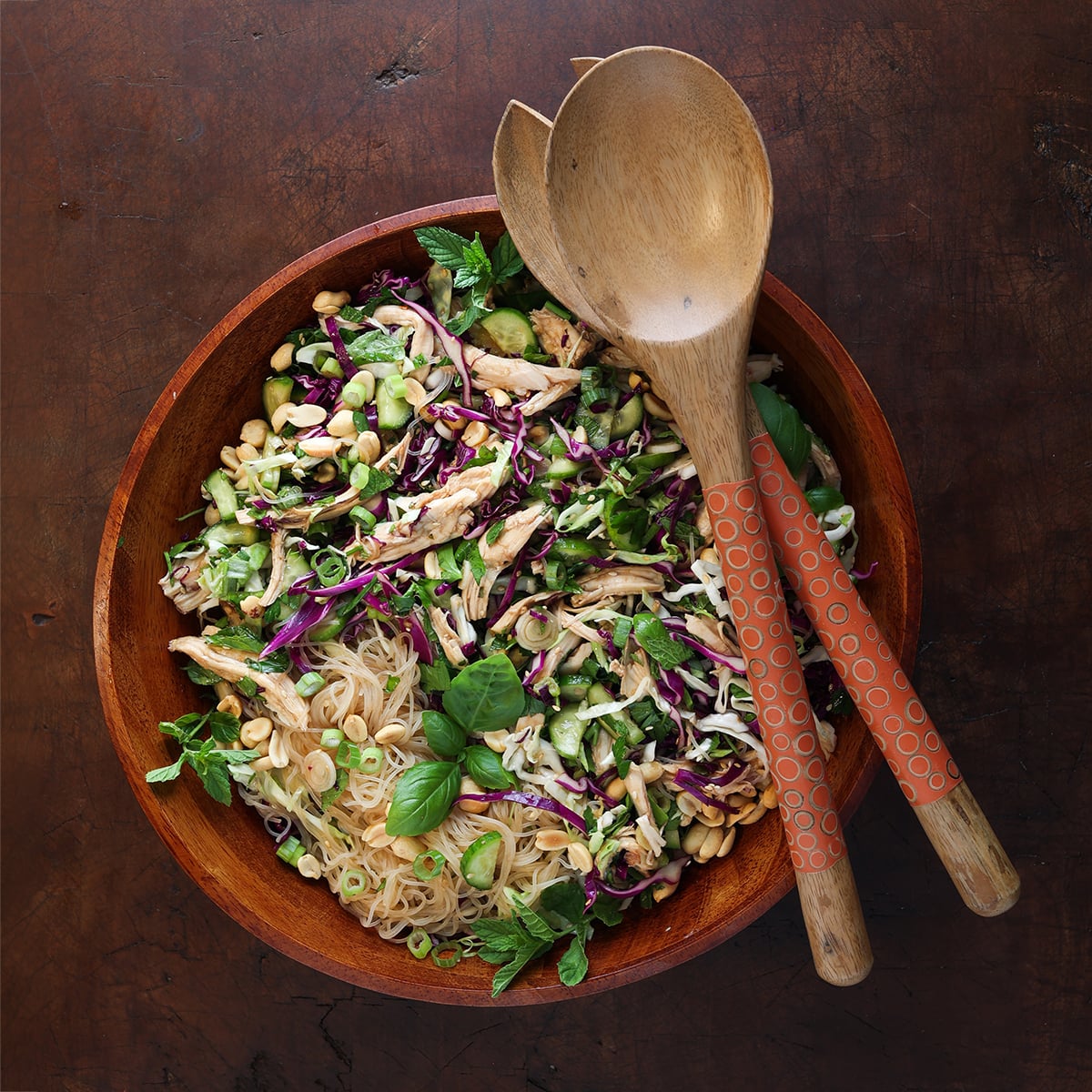 Top view of a Vietnamese chicken vermicelli salad with fresh herbs in a large wooden bowl.