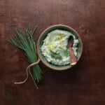Herbed goat cheese served in a bowl with fresh chives laying next to the dish.
