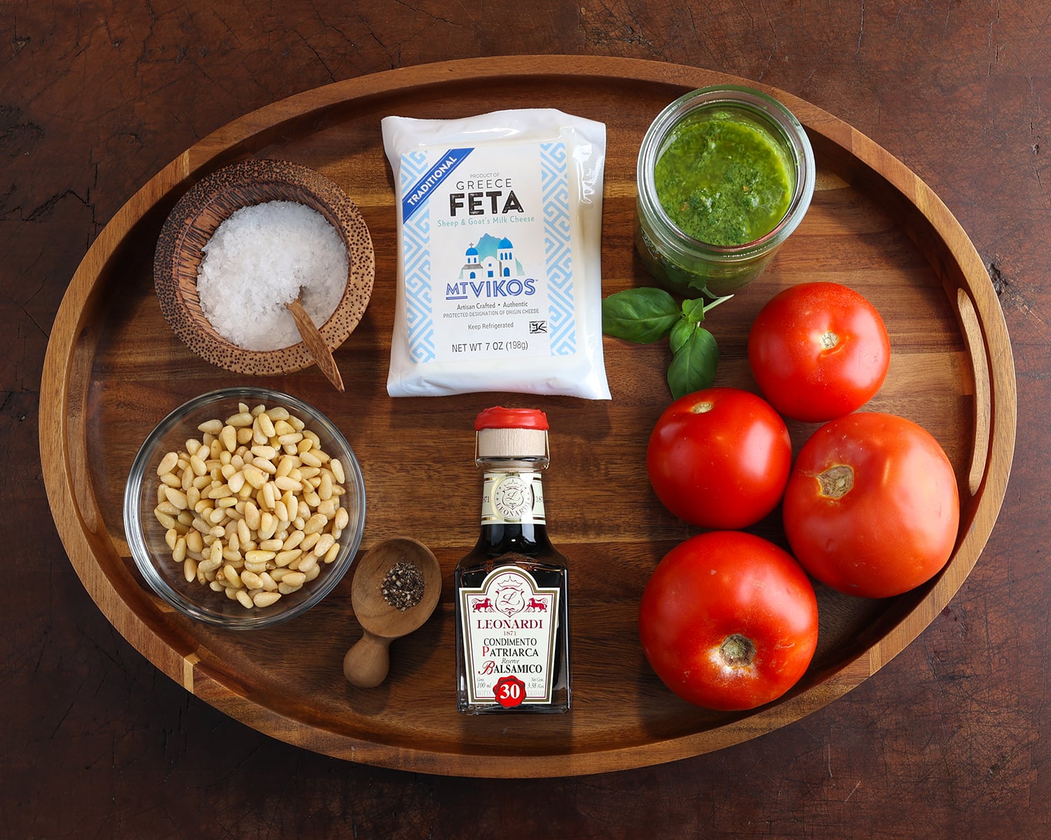 Ingredients laid out on a wooden tray to make summer tomato carpaccio and a jar of homemade basil vinaigrette.