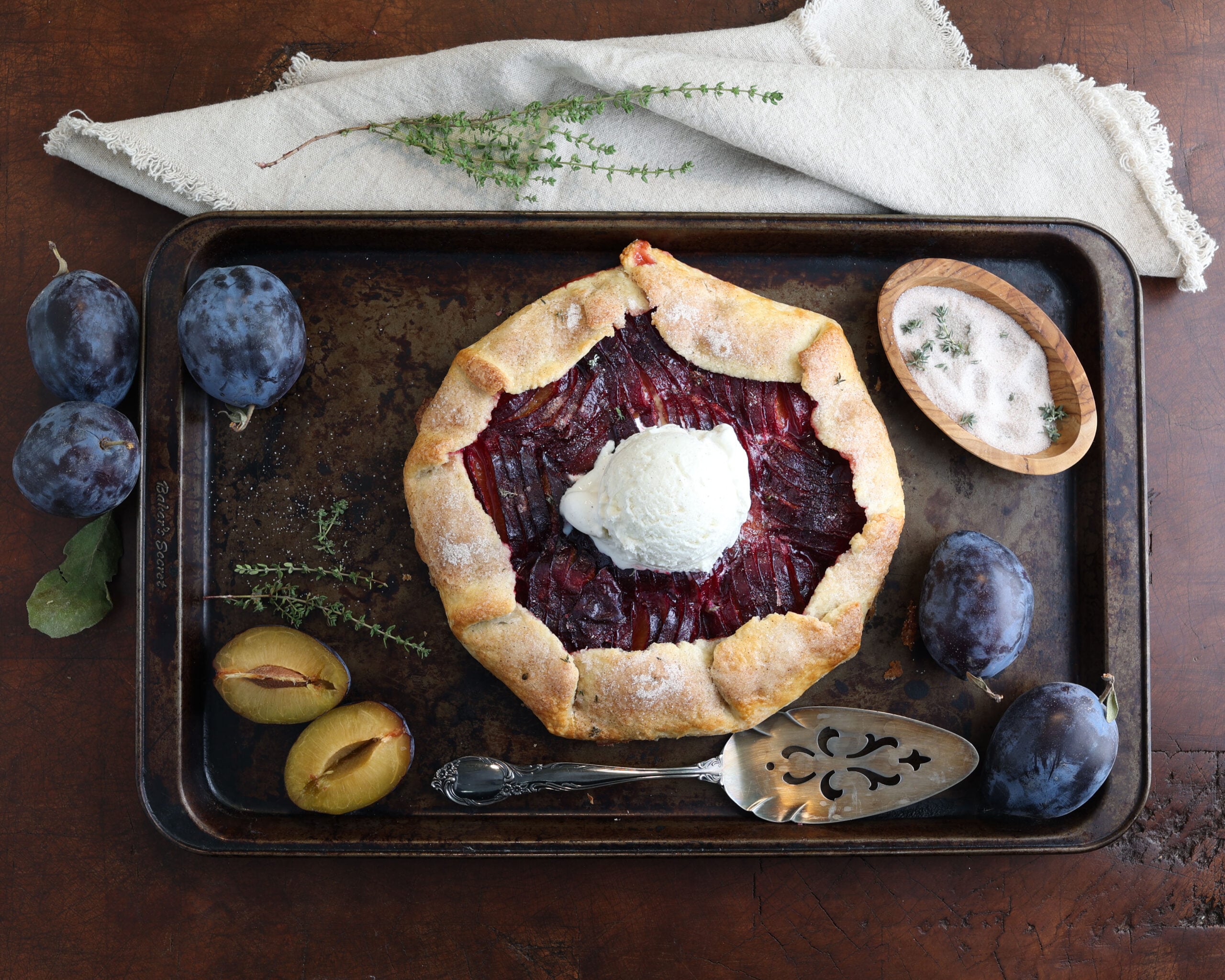 fully baked gallete on a rutic pan with plums and thyme along the sides and a scoop of ice cream on top.