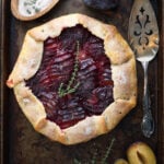 plum galette with sprigs of thyme on top and a pie server to the side
