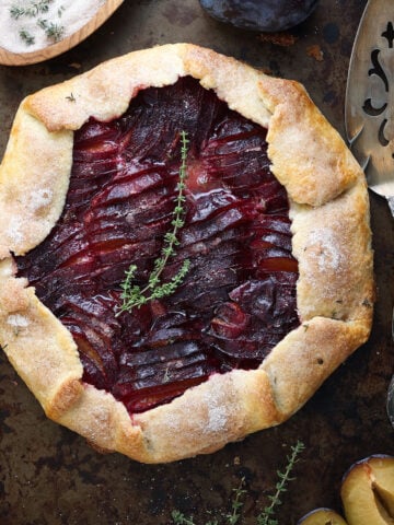 plum galette with sprigs of thyme on top and a pie server to the side