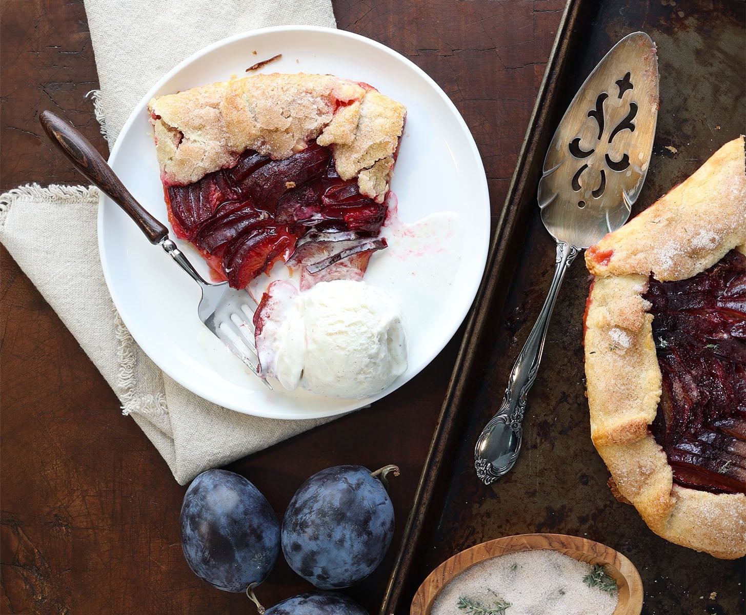 Slice of plum galette on white plate on napkin with cut galette to the side