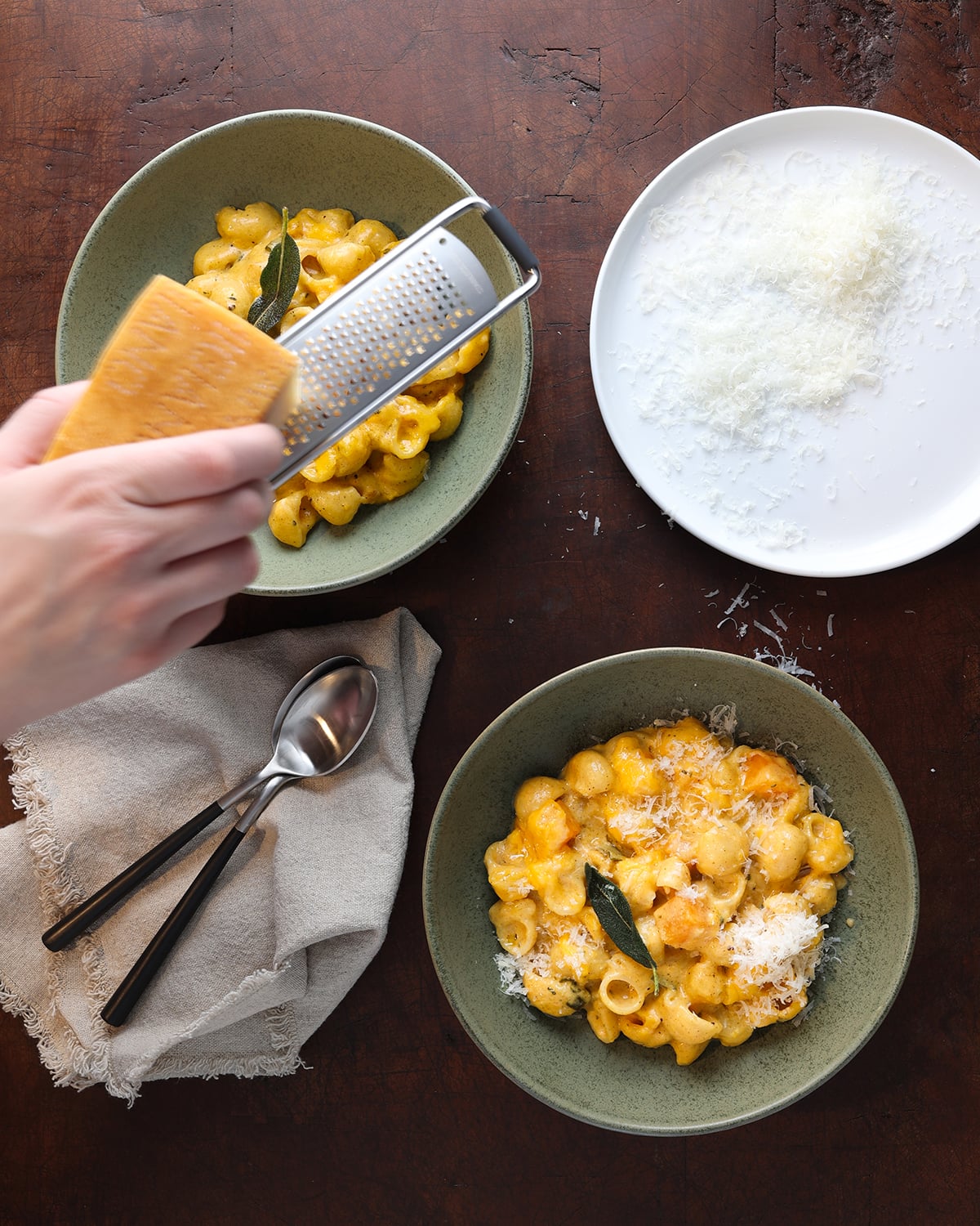 Hand grating parmesan cheese over a bowl of butternut squash mac and cheese.