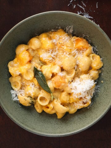 A sage leaf garnished over a bowl of butternut squash mac and cheese.