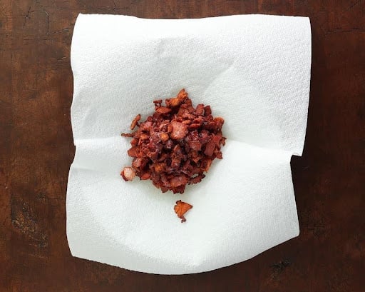Crispy chopped bacon resting on a paper towel lined plate.